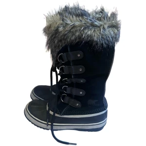 Svarta vinterstövlar från Sorel med fuskpäls - Säljer ett par svarta vinterstövlar från Sorel med fuskpäls upptill och snörning framtill. Stövlarna har en robust platt sula i naturgummi och detaljer i skinn och mocka. Perfekta för kalla dagar med sin höga modell och fluffiga kant.