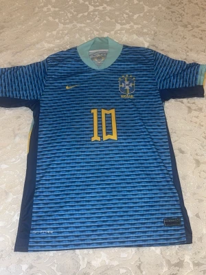 Brasilien Neymar jr.  tröja  - Säljer en blå Brasilien fotbollströja från Nike med Neymar Jr. och nummer 10 på ryggen. Tröjan har vågigt mönster, gula detaljer och ljusblå krage. Tillverkad i Dri-FIT material som andas, perfekt för fotboll eller träning.