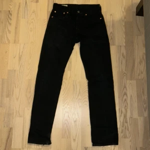 Svarta Levi's 501 jeans 28/32 - Svarta Levi's 501 jeans med klassisk rak passform och knäppning fram. Jeansen har fem fickor, läderpatch bak. Ny pris 1100kr, bra skick, lite slitna längst ner.