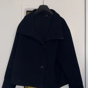 Marinblåa  kappa från Gina Tricot - Säljer en marinblå kappa från Gina Tricot i storlek XS. Jackan har bred krage, dubbelknäppning med stora knappar och en rak, lite boxig passform. Perfekt för dig som vill ha en klassisk och stilren look till höst och vinter.