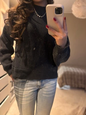 Mörk grå stickad tröja med ribbad struktur - Säljer en mörkgrå stickad tröja med ribbad struktur och hög hals. Tröjan har långärmade och en loose passform som gör den riktigt skön att bära. Perfekt att matcha med jeans eller kjol för en chill och snygg look.