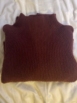 Burgundy färgad  stickad polotröja från Kappahl - Mysig brun/röd stickad polotröja från Kappahl i storlek S. Tröjan har ribbad struktur och lång ärm, perfekt för kyliga dagar. Den har en hög krage som ger extra värme och en chill vibe. Passar dig som gillar klassisk stil med en twist.