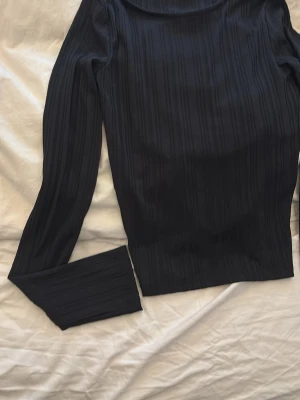 Svart långärmad topp från Nelly XS - Säljer en svart långärmad topp från Nelly i storlek XS. Toppen har ett diskret randigt mönster, öppen rygg med snörning och knyt bak. Materialet känns mjukt och stretchigt, perfekt för att skapa en cool look.