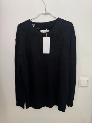 Svart stickad tröja Maison Margiela storlek S - Svart stickad tröja från Maison Margiela med klassisk rund halsringning och ribbade muddar. Tröjan har långa ärmar och den ikoniska vita sömmen bak i nacken. Perfekt för lager-på-lager under kyliga dagar. Storlek S