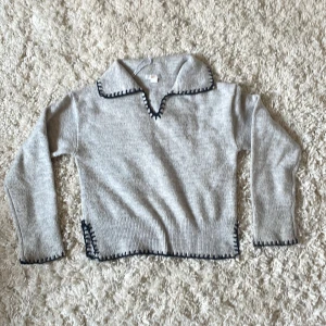 Grå stickad tröja med krage från Gina Tricot - Säljer en ljusgrå stickad tröja från Gina Tricot med stor krage och mörkblå dekorativ kant runt krage, ärmslut och nederkant. Tröjan har lång ärm och en avslappnad passform. Säljer för att den har ett sticksigt material och har själv rätt så känslig hud. Snygg till jeans. Orginalpris ca 250kr. 