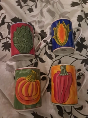 Färgglada keramikmuggar – 4-pack med grönsaksmotiv - Säljer ett set om fyra fina muggar med handmålad känsla och färgstarka motiv: kronärtskocka, majs, pumpa och paprika. Perfekta till kaffe, te eller som dekoration i köket.  * Rejäla muggar i keramik * Alla i mycket fint skick * Matchande serie * Härliga, klara färger  Perfekt för dig som gillar unika och charmiga köksdetaljer!  Skickas via posten men köpare står för frakten. Vid övriga frågor skicka gärna meddelande.  Lämnar självklart god omdömen om köparen gör det.  Inget återköp eller retur o