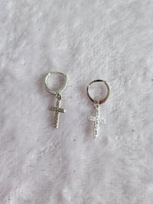 Små hoops med kors i äkta silver från Glitter  - Örhängen i äkta silver från Glitter med kors. Använda en del. Fortfarande fint skick. Nypris 299 kr.