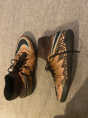 Nike Hypervenom X fotbollsskor - Säljer ett par Nike Hypervenom X retro  fotbollsskor i brons och svart med turkosa detaljer. Skorna har högt stickat skaft, snörning och grafiskt mönster på sidorna. Yttersulan är svart med turkos Nike-logga och har mönstrad struktur för bra grepp på planen.Ps svåra att få tag på .