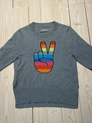Grå stickad cashmere tröja från ZADIG & VOLTAIRE - Säljer en grå stickad tröja från ZADIG & VOLTAIRE med ett stort broderat peace-tecken i regnbågens färger på bröstet. Tröjan har långa ärmar, rund hals och diskret ZV-detalj på sidan. Perfekt för dig som gillar färg och coola prints. Tröjan är 100% CASHMERE, dvs toppen kvalitet. NÄSTAN HELT OANVÄND!!