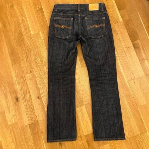 Nudie Jeans Bootcut Ola dry - Säljer ett par sjuka vintage Bootcut Ola från nudie jeans som är en modell som slutade tillverkas för flera år sedan. De är dry och knappt tvättade i mycket gott skick. Storlek efter lapp - 31/32. Mått: Längd 101cm, Midja 38cm, Benöppning 22cm. Hör av dig vid minsta lilla!