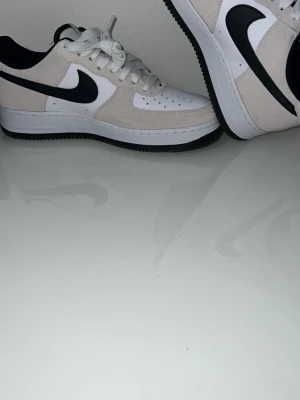 Nike Air Force 1  - Nike Air Force 1 sneakers i vitt och beige med svart swoosh. Säljer dessa skor använt bara 1 gång och har inga skavanker och ör i perfekt skick 
