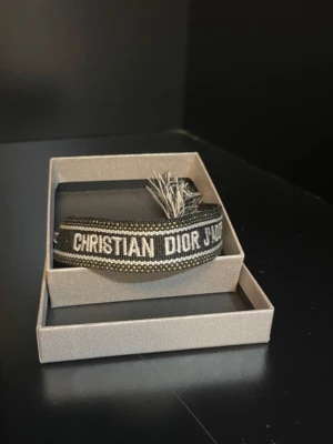 Svart och vit Christian Dior  - Säljer en svart och vit  från Christian Dior med tydlig logotyp i vitt. ett band med snörning och tofsar i ändarna, vilket ger en cool och unik look. Materialet är stickat och känns mjukt mot huden. Perfekt för dig som vill ha något extra till outfiten.