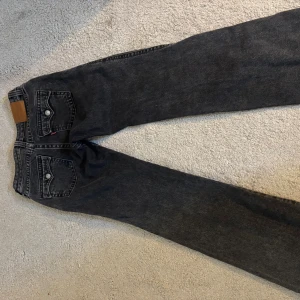Levi's 501 svarta jeans straight fit - Säljer ett par klassiska Levi's 501 jeans i svart tvätt. De har raka ben, fem fickor och knappgylf. Jeansen är tillverkade i kraftigt bomullsdenim och har den ikoniska läderlappen bak i midjan. Perfekta för dig som gillar en tidlös och clean look.