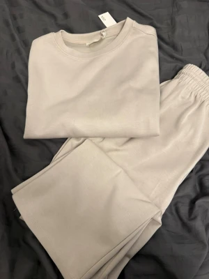 Beige mjukisbyxor och tröja från 157 - Säljer ett par beige mjukisbyxor och en tröja  från 157 med elastisk midja och raka ben. Byxorna är gjorda i mjukt bomullsmaterial och har en clean, enkel look som är perfekt för chill dagar. Färgen är ljusbeige och materialet känns riktigt skönt mot huden. Tröjan ny (byxorna använda en gång)