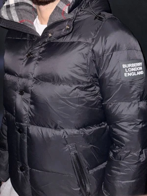 Svart Burberry pufferjacka med huva - Helt ny oanvänd svart pufferjacka/väst från Burberry. Tagg står kvar och originalpåse medföljer.