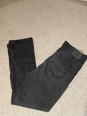 Svarta Lee jeans straight fit 14-15Y - Säljer ett par svarta jeans från Lee i rak modell. Klassisk femficksdesign, knapp och dragkedja fram. Jeansen har en diskret tvättad look och passar dig som gillar en enkel och clean stil. Märkta med Lee-logga på bakfickan.