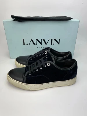 Lanvin svarta sneakers i sammet och skinn - Lanvin sneakers med svart sammet på sidorna och svart skinn på tån. Klassisk rund tå och platt vit sula. Svarta snören och metallöglor ger en clean look. Perfekt för dig som gillar stilrena och lyxiga sneakers med exklusiv känsla.