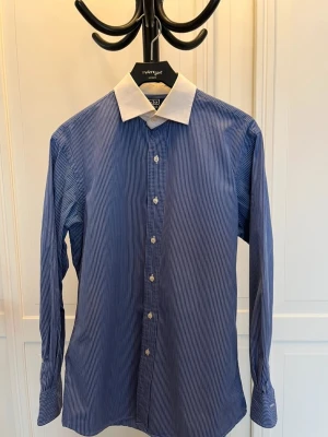 Blårandig skjorta Polo Ralph Lauren - Snygg blårandig skjorta från Polo Ralph Lauren, modell Regent Custom Fit. Skjortan har vit klassisk krage, långa ärmar och knappar framtill. Tillverkad i mjuk bomull som känns skön mot huden. Perfekt för dig som gillar stilrena och tidlösa plagg. Finns inga defekter, då jag säljer vidare eftersom det passar för stort för mig. Tyvärr ingen kvitto, fick den av en polare