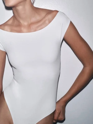 Vit offshoulder bodysuit från ZARA - Säljer en stilren vit bodysuit från ZARA i storlek L men passar M. Modellen har offshoulder och är ärmlös med en clean, tight passform. Materialet är mjukt och stretchigt, perfekt för att skapa en snygg siluett. Enkel och modern design utan detaljer eller mönster. Helt ny