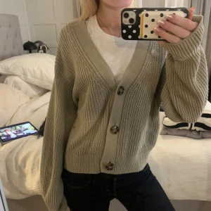 Grön stickad kofta från H&M - Säljer en grön stickad kofta från H&M i storlek S. Koftan har grovstickad struktur, stora mörka knappar framtill och en djup v-ringning. Modellen är loose fit med långa ärmar och breda muddar. Perfekt att slänga över en t-shirt för en chill look.