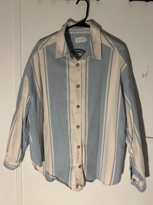 Randig blå och vit skjorta från Topman - XL - Säljer en skjorta från Topman i storlek XL. Skjortan är blå och vit med breda vertikala ränder, har klassisk krage och knappar framtill. Materialet känns som bomull och är mjukt mot huden. Perfekt för dig som gillar relaxed och loose fit. Funkar perfekt både som vanlig skjorta och overshirt.
