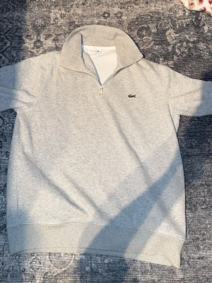 Grå half zip tröja från Lacoste - Grå Lacoste quarter Zip perfekt nu säljer även en vit just Nu om man köper fler än 1 produkt hos mig får man rabbat. Den är helt ny, Finns inte bättre kvalité än detta på marknaden