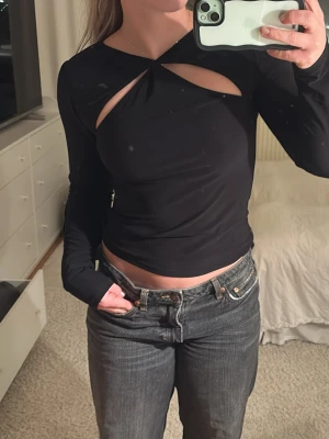 Svart långärmad topp med cut-outs - Säljer en svart långärmad topp med coola cut-outs fram och öppen rygg. tillverkad i ett stretchigt syntetmaterial. Perfekt för dig som gillar trendiga detaljer och vill sticka ut lite extra.