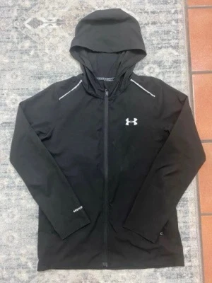 Under armour jacka - Svart vindjacka från Under Armour med huva och hel dragkedja framtill. Jackan har vita detaljer vid axlarna och logga på bröstet. Perfekt för dig som gillar sportig stil och vill ha något lätt och funktionellt.