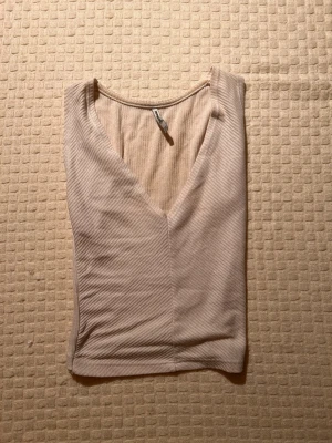 Beige ribbad linnetopp från Stradivarius - Säljer en beige ribbad linnetopp från Stradivarius i storlek L. Toppen har v-ringad hals och är ärmlös med en croppad passform. Materialet är mjukt och stretchigt, perfekt för varma dagar. Snygg att styla med jeans eller kjol!
