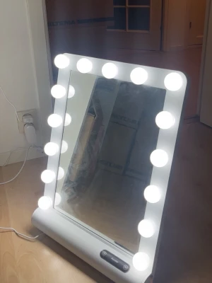Sminkspegel med LED-lampor från Auxmir - Säljer en vit sminkspegel med 12 runda LED-lampor runt ramen. Spegeln har touch-knappar för att justera ljuset och står stadigt på en platt bas. Perfekt för att få till rätt belysning när du sminkar dig. Strömkabel medföljer.