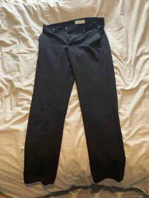 Svarta kostymbyxor  - Svarta kostymbyxor från Supply Project med klassisk rak passform. Byxorna har bälteshällor, knapp och dragkedja i midjan samt bakficka med knapp. Materialet är mjukt och har en lätt stretch för extra komfort.