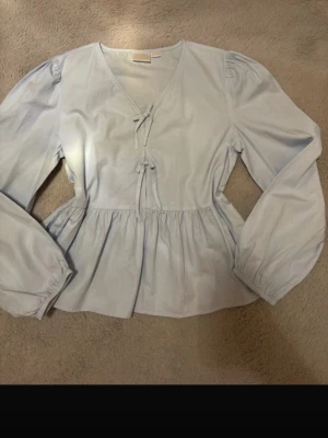 Ljusblå blus med knytdetaljer - Söt blus från ginas barnavdelning i storlek 170. Använd 1 gång för den är lite för stor. Knytarna går ej att knyta upp