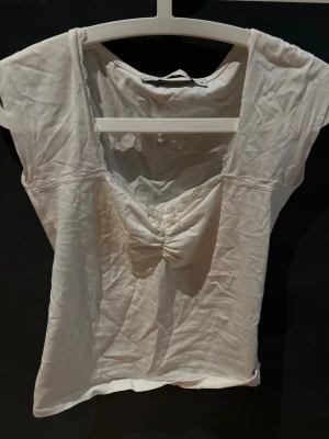 Vit linnetopp med spetsdetaljer - Säljer en vit linnetopp från Lager i storlek M. Toppen har spetsdetaljer längs halsringningen och en snygg rynkning framtill. Modellen är ärmlös och har en feminin v-ringad form som ger en fräsch och enkel look.