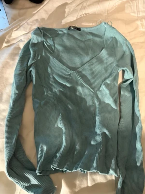  Ribbad långärmad topp💙🦋🐬✨ - Säljer en ljusblå/turkos ribbad topp från Gina Tricot med v-ringad hals och dekorativa sömmar framtill. Toppen är långärmad och har en slim passform som sitter snyggt på kroppen. Perfekt att styla med jeans eller kjol för en fräsch look.🐬🌟