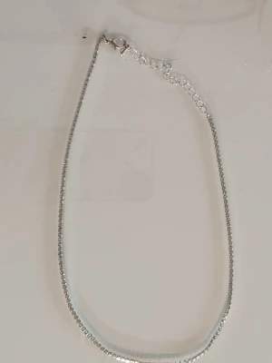 Silverfärgad glittrig halsband - Säljer en snygg silverfärgad väst med glittriga detaljer. Västen har en klassisk rak form och är tillverkad i syntetmaterial som ger en skimrande look. Perfekt för dig som vill sticka ut med en cool och modern stil. Passar dig som gillar att addera lite extra bling till outfiten. Fått den av min syster så vet ej var den är ifrån men möjligtvis H&M.