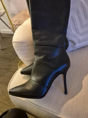 High heels svarta höga skinn stövlar med klack - Säljer ett par svarta höga skinnstövlar med spetsig tå och smal hög klack. Skorna är tillverkade helt i skinn och har en stilren, elegant design som passar perfekt till en trendig outfit. Snygga detaljer och klassisk form gör dem till ett måste i garderoben. Hel dragkedja i sidan. Påsatt extra sula. Mycket bekväma att gå i. Aldrig använda.