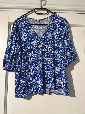 Blå blommig blus från Happy Holly - Blommig blus i storlek 36/38 från Happy Holly. V-ringad och trekvatslång ärm.