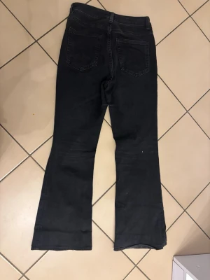 Svarta bootcut jeans med hög midja - Säljer ett par svarta jeans med bootcut-snitt och hög midja. Jeansen har klassiska fem fickor, bälteshällor och knappstängning fram. Materialet är jeans och färgen är mörk svart, vilket ger en snygg och stilren look.