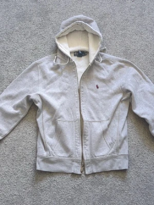 Grå Ralph Lauren Zip Hoodie - Grå Ralph Lauren Zip Hoodie som jag köpt här på plick😁 Tröjan är använd 5-10 så länge jag haft den. Det mindre bra är fläckarna som tidigare ägare har lämnat, därav priset. Men det är inget som syns eller som man tänker på. Tröjan är skön och är i storlek Medium. Skriv gärna om ni har mågra funderingar!