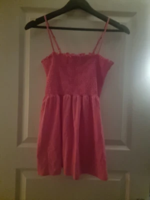 Rosa smockad linnetopp med volang - Säljer en söt rosa linnetopp med smockad överdel och tunna axelband. Toppen har en volangkant upptill och ett rynkat, luftigt fall nedtill. Perfekt för varma dagar och enkel att matcha med jeans eller kjol.