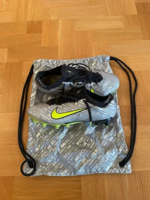 Nike Air Zoom Mercurial Vapor 15 Elite Ag-Pro XXV - Ett par Nike Mercurial fotbollsskor i bra skick, med tillhörande påse. Enda tydligt synliga deffekterna på utsidan är slitningar på sulan och slitning på ena Swoosh-loggan, se bild. Storlek: EUR 43