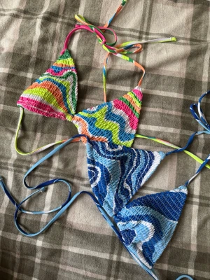 Färgglad vågmönstrad bikiniöverdel - Säljer en bikiniöverdel med vågigt mönster i starka färger som blå, grön, rosa, orange och vit. Triangelformade kupor med smockad struktur och tunna knytband i matchande färger. Perfekt för dig som vill sticka ut på stranden! 2 för 1 pris 