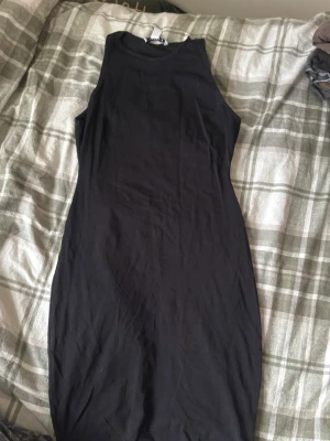 Svart ärmlös klänning NLY Trend - Säljer en svart, figurnära klänning från NLY Trend i storlek M. Klänningen är ärmlös med hög hals och har en enkel, stilren design. Materialet är mjuk bomull som känns skönt mot huden. Perfekt för dig som gillar minimalistisk stil.