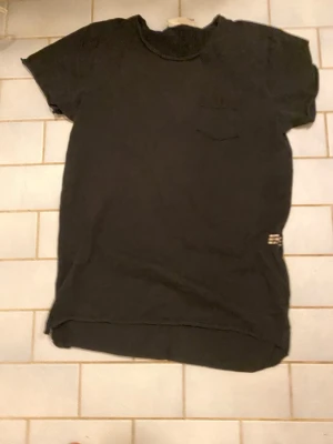 Svart t-shirt med ficka - Svart t-shirt i mjuk bomull med rund hals och korta ärmar. En liten bröstficka på vänster sida och diskret etikett vid nederkanten. Enkel och clean design som funkar till jeans eller shorts.