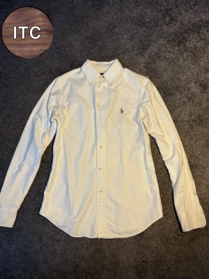 Vit skjorta från Polo Ralph Lauren XS - Säljer en vit skjorta från Polo Ralph Lauren i storlek XS, custom fit. Skjortan har klassisk krage, knappar hela vägen och den ikoniska broderade polospelaren på bröstet. Materialet är mjuk bomull och modellen är långärmad med normal passform.