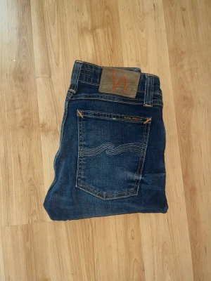 Nudie Jeans - Snygga mörkblå skinny lin jeans från Nudie Jeans med kontrastsömmar. Modellen har en skinny passform. Midja 30cm, längd 100cm. JAG SKICKAR EJ FLER BILDER NÄR JAG BÄR JEANSEN! för bättre inblick i passformen rekommenderar jag att googla på modellnamnet. För storleksguide kolla måtten noggrant då jeansen alltid kan vara uppsydda heller krympta och jag ej tar emot returer :) s5,3