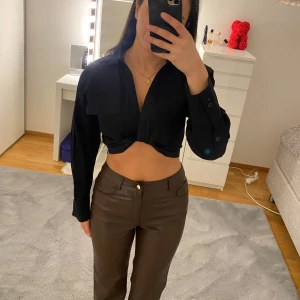 Svart croppad skjorttopp - Säljer en svart croppad skjorttopp med lång ärm och krage. Toppen har två stora bröstfickor och knäppning framtill. Perfekt för dig som gillar en edgy och trendig look. Passar till både jeans och kjol.