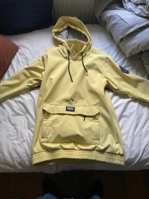 Skidjacka från dope snow - Säljer en ljusgul vindjacka från Dope Snow med stor magficka, huva med snörning och svart patch på ärmen. Jackan har elastisk nederkant och är tillverkad i ett slätt syntetmaterial. Perfekt för dig som vill sticka ut med en clean look. Använd en vecka inga skador på jackan. Kan gå lägre i pris vid snabb affär. 