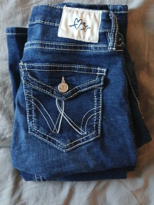 Blå jeans från Gina Tricot med kontrastsömmar - Snygga blå jeans från Gina Tricot i storlek 164. Jeansen har vita kontrastsömmar, klassisk femficksdesign och dekorativ knapp på bakfickan. Materialet är jeans och passformen är normal. Perfekt för dig som gillar stilrena detaljer.