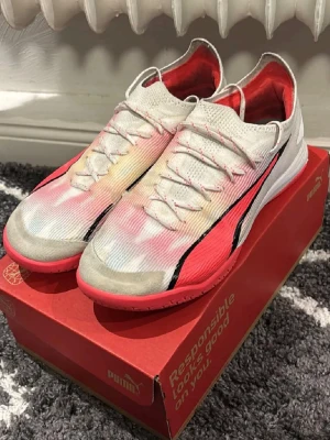 Puma inomhusskor  - Säljer ett par Puma fotbollsskor i storlek 42.5. Skorna har en vit ovandel med röda och svarta detaljer, samt en röd sula. Skorna är lite skadade men funkar bra.